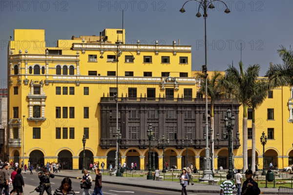 Yellow colonial building with wooden balcony on a busy street with strolling people, the historic center of Lima in Peru
