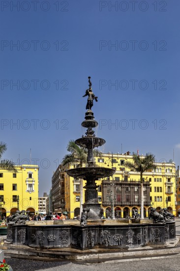 Historic fountain in a square with yellow buildings and palm trees under a blue sky, The historic center of Lima in Peru
