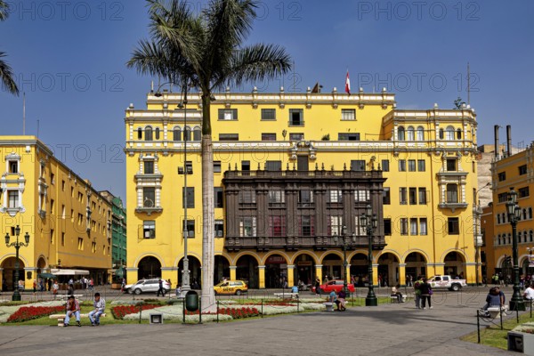 Wide square with yellow colonial buildings and palm trees surrounded by people and cars, The historic center of Lima in Peru