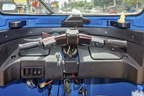 The picture shows the cockpit of a blue car rickshaw in an urban environment, the cockpit of a tuk tuk