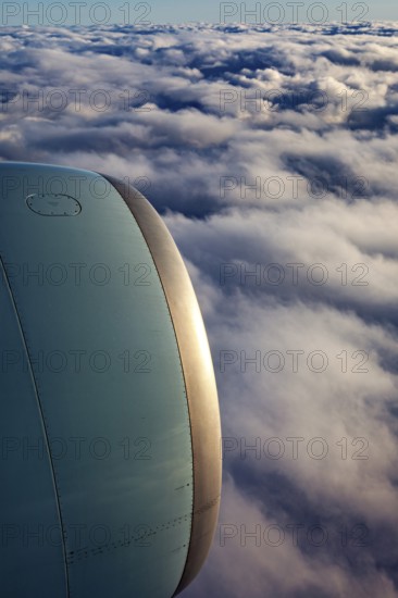 Airplane engine towering over clouds that glow at dusk, On an airplane above the clouds