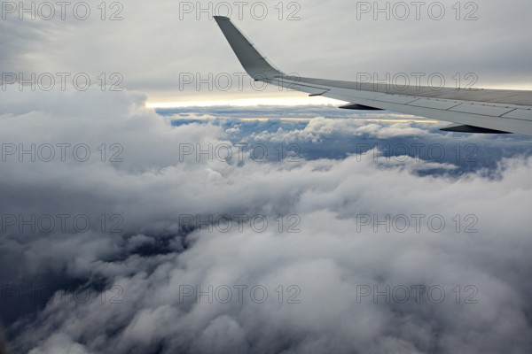 View of airplane wings above a thick cloud cover in the sky, In an airplane above the clouds