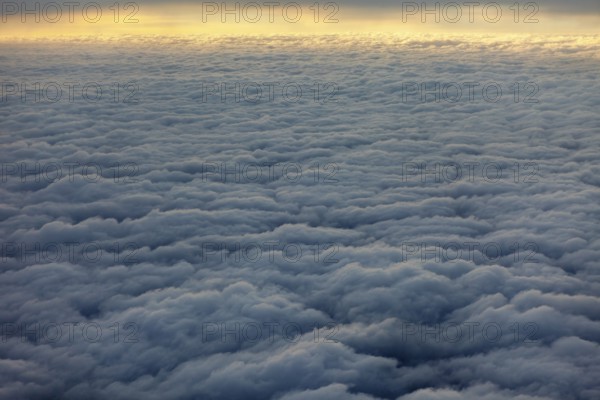 Dense, wavy cloud cover in grey sky, above the clouds on an airplane
