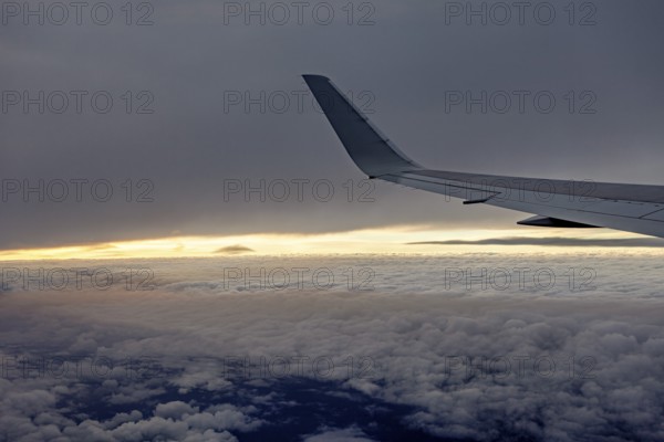 View of airplane wings at sunset over clouds, In an airplane above the clouds