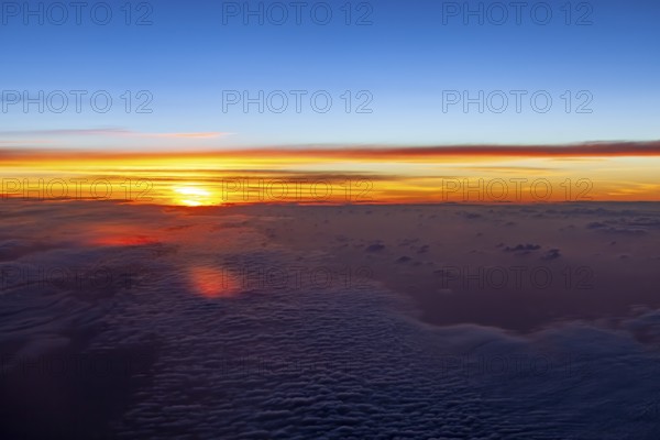 Bright colors of a sunrise over a cloud cover in the sky, on an airplane above the clouds
