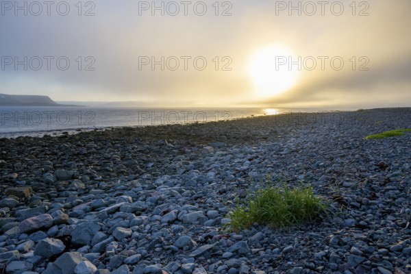 A peaceful beach at sunset with rocks and calm sea under a slightly cloudy sky, Båtsfjord, Finnmark, Norway