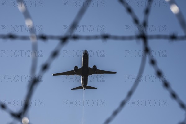 Symbolic picture security at the airport, outer fence at Düsseldorf International Airport, steel wire fence, with S-wire rollers, NATO wire, on the fence crown, airplane taking off, North Rhine-Westphalia, Germany