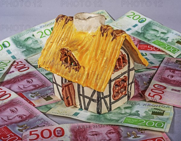 Small decorative ornamental cottage standing on Swedish 500 and 200 kronor banknotes. Symbol image