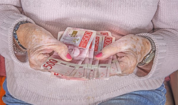 An elderly woman's hands holding Swedish 500-krona banknotes
