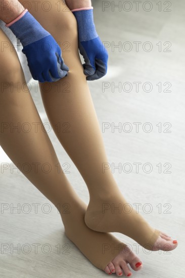 A woman sits at home and puts on medical compression stockings with special gloves on