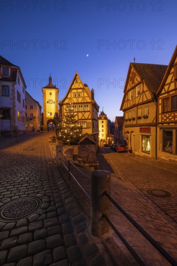 December 25, 2025: Christmastime at Plönlein — Rothenburg ob der Tauber, Bavaria, Germany. Festive Christmas tree and city lights at blue hour with moon in the sky