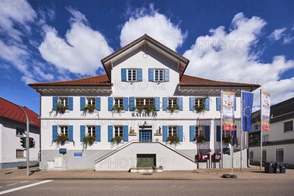 Town Hall, flags on flagpoles, 750 years of Gutach Schwarzwaldbahn, The home of the Bollenhut, ... always goes, 1275 - 2025, European flag, façade with windows and shutters, flower boxes, double stairway, blue sky, cumulus clouds, main road B33, Gutach Schwarzwaldbahn, Black Forest, Ortenaukreis, Baden-Württemberg, Germany