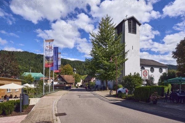 St. Peter and Paul parish church, church tower, flag on the flagpole, 750 years Gutach Schwarzwaldbahn, the home of the Bollenhut, ... always goes, general architecture, Black Forest house, hill, hilly landscape with coniferous forest, zone 30 sign, road, blue sky, cumulus clouds, Kirchstraße, Gutach Schwarzwaldbahn, Black Forest, Ortenaukreis, Baden-Württemberg, Germany