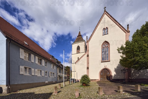 St. Martin parish church, neo-Gothic style, church tower, church tower clock, flagpoles, barrier bollards, entrance door, church window, residential buildings, multi-family houses, pointed roof, façade with windows and shutters, blue sky, cumulus clouds, Kirchstraße street, Staufen im Breisgau, Black Forest, Breisgau-Hochschwarzwald district, Baden-Württemberg, Germany
