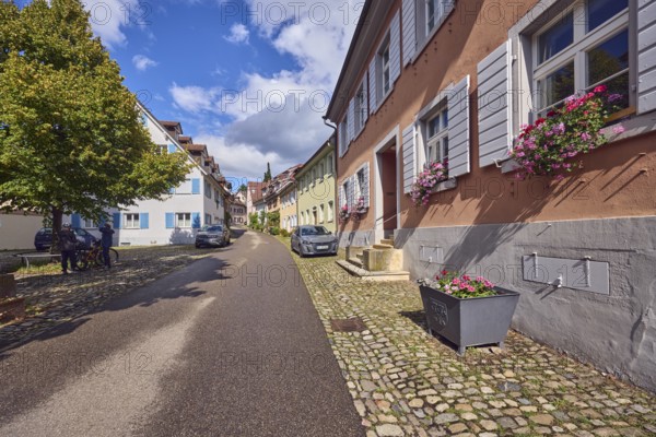 Residential buildings, apartment buildings, houses, general architecture, façade with windows and shutters, entrance, staircase, flower boxes, flower pots, tree, cars, wet road, blue sky, cumulus clouds, stratocumulus clouds, white and dark clouds, St.-Johannesgasse alleyway, Staufen im Breisgau, Black Forest, Breisgau-Hochschwarzwald district, Baden-Württemberg, Germany