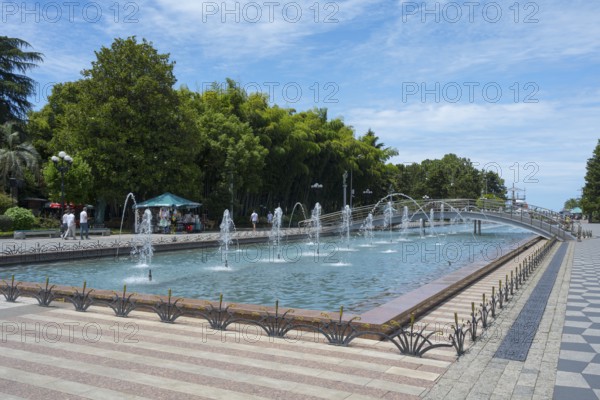 Fountain with walkway and trees in urban landscape under blue sky, Batumi Boulevard, Batumi, Black Sea, Ajara region, Adjara, Autonomous Republic, Georgia