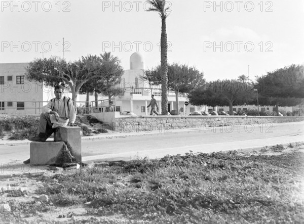 Young man sitting on low wall on street, Tripoli, Libya, North Africa 1956