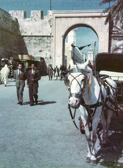 Horse drawn taxi in foreground, people walking in street, Bab al-Khendig archway city gate, Tripoli, Libya, North Africa 1956