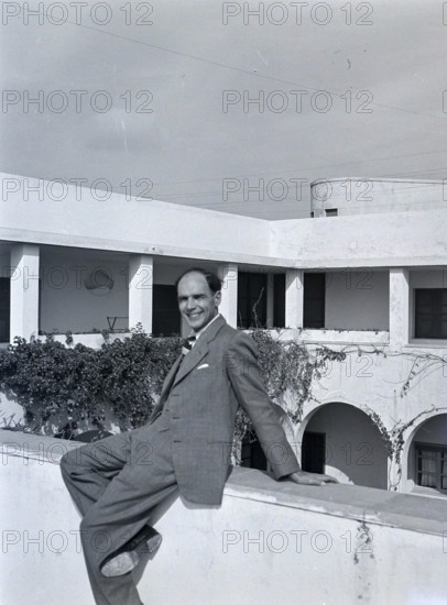 Smartly dressedBritish man sitting on hotel wall of Arabic style building, Tripoli, Libya, North Africa 1956