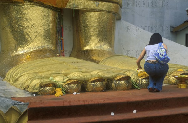 A young woman places flowers on the toes of the standing Buddha at Wat Indrawihan, Bangkok, Thailand, December 2002, vintage, retro, old, historic