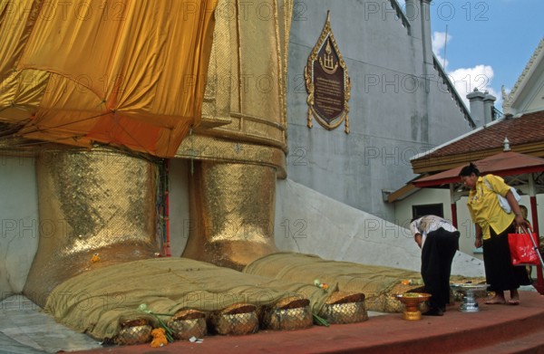 Women place flowers on standing Buddha's toes at Wat Indrawihan, Bangkok, Thailand, December 2002, vintage, retro, old, historic