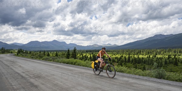Young woman riding a bicycle on a dirt road through the tundra, mountainous landscape, Denali Park Road, Denali National Park and Preserve, Alaska, USA