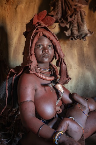 Himba woman sitting with baby in traditional hut, Himba village, Kaokoveld, Kunene, Namibia