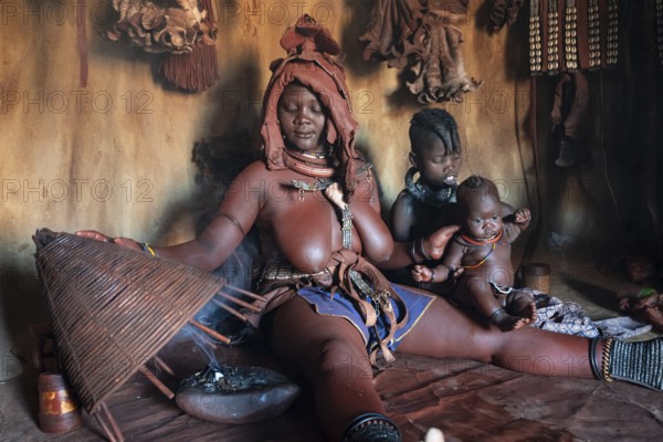 Himba woman sitting with baby, Himba perfume, scented smoke from burning plants, Himba village, Kaokoveld, Kunene, Namibia