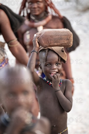 Himba woman and children run to fetch water with canisters through dry countryside, traditional Himba, Kaokoveld, Kunene, Namibia