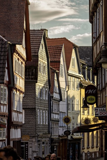 Narrowly built street with historic half-timbered houses and people passing by in the evening light, The historic old town of Marburg an der Lahn in Hesse