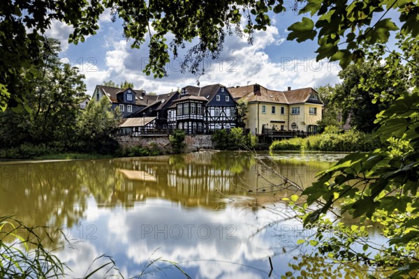 Half-timbered houses on the lakeside with blue sky and clouds, surrounded by trees, The historic houses of Marburg are reflected in the Lahn in Hesse