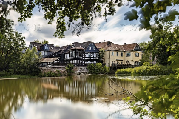 Half-timbered houses are reflected in the quiet lake, surrounded by lush vegetation. The historic houses of Marburg are reflected in the Lahn in Hesse