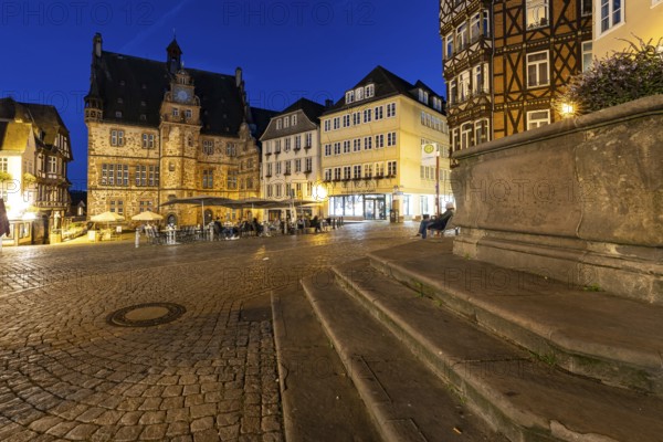 Square with historic flair, surrounded by half-timbered architecture, in the evening with paved floors and stairs in the foreground, The old town hall of Marburg at blue hour