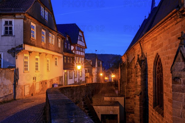 A nocturnal old town with half-timbered houses and cobblestones, warm lantern light creates a historic atmosphere, At the blue hour in Marburg city center in Hesse
