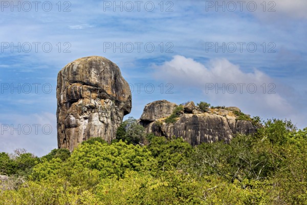 An impressive rock formation rises high above a green forest under a partly cloudy sky, the landscape of the Yala National Park Sri Lanka