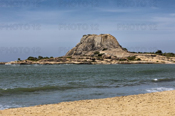 Tranquil coastal landscape with a large rock in the sea, surrounded by sandy beach and blue sky, the scenery of Sri Lanka's Yala National Park