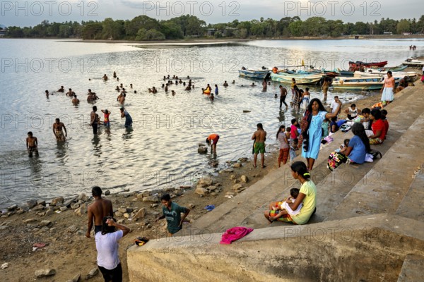 Children and adults on the riverbank, some bathe while others enjoy the view on the boats, people at a lake in Sri Lanka