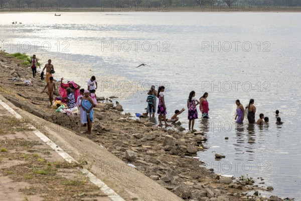 A group of people on the riverbank, some in water, others sitting or standing on a stone bank, people at a lake in Sri Lanka