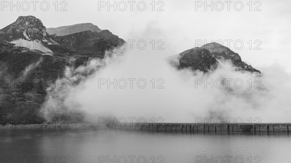 Fog rises over the dam of the Lac de Moiry reservoir, black and white photo, Val d'Anniviers, Valais Alps, Canton of Valais, Switzerland