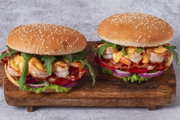Two shrimp burgers and buns with sesame seeds, bacon, lettuce, tomatoes and onions, On a wooden board