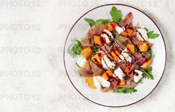 Salad with slices of ripe melon, prosciutto, mozzarella and fresh arugula, decorated with balsamic glaze