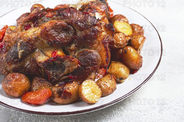 Pork knuckle baked with vegetables, new potatoes, on a white plate, homemade, no people