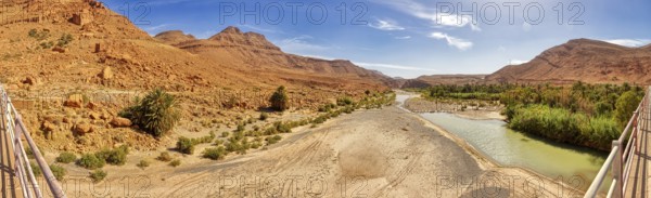 River crosses a barren desert landscape with scattered green plants, Morocco, Achbaro-River Ziz, panorama