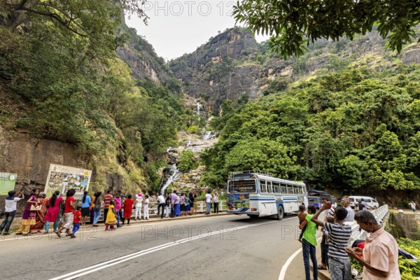 Mountain road with a bus and people looking at a waterfall surrounded by green mountain scenery, tourists at waterfalls in the mountains near Kandy in Sri Lanka