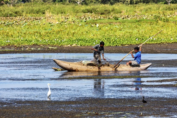 Two children navigate with a paddle through calm waters, nestled in a natural and green landscape, fishermen on a lake near Kandy in Sri Lanka