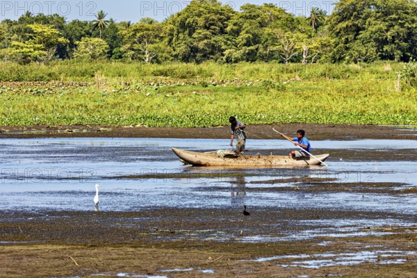 Two children paddle in a small boat on a quiet river surrounded by lush greenery and peaceful nature, fishermen on a lake near Kandy in Sri Lanka