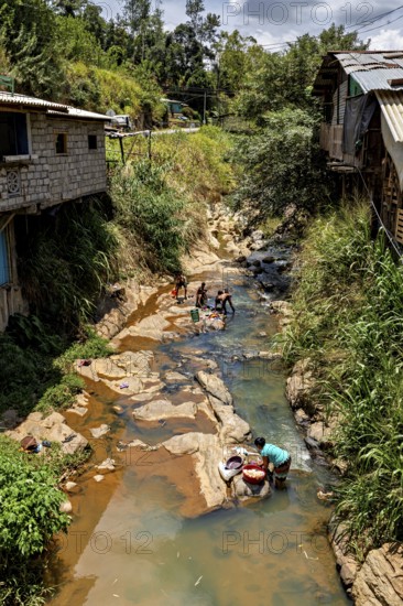 People wash clothes on a shallow river between simple village buildings and lush vegetation, woman wash clothes in a river in the mountains near Kandy in Sri Lanka