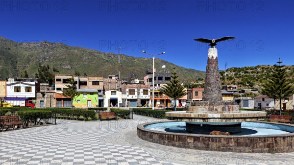 A public square with fountain and bird statue, surrounded by colorful houses and mountains, the town of Colca in Peru