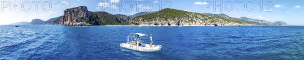 Motor boat off picturesque rocky coast, cliffs and Cala Luna beach, aerial view, Golfo di Orosei, Baunei, Sardinia, Italy