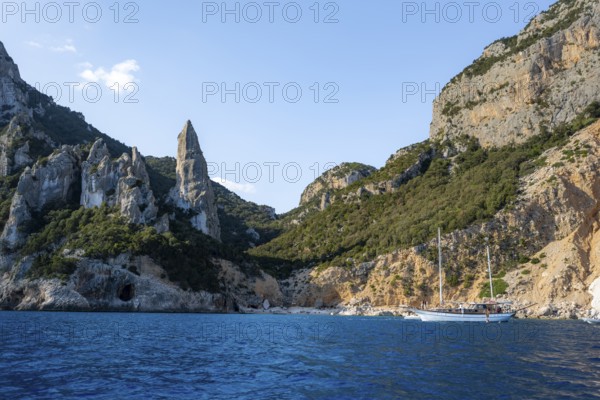 Excursion boat off picturesque rocky coast, cliffs in morning light, L'Aguglia pinnacle, blue sea and Cala Goloritzé beach, Golfo di Orosei, Baunei, Sardinia, Italy